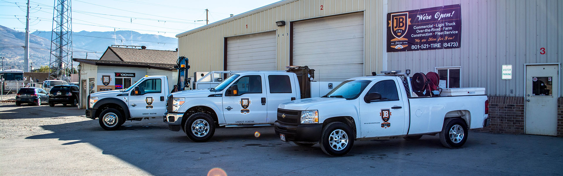 JB Tire service trucks parked at the West Bountiful shop with mountains behind the garage bays